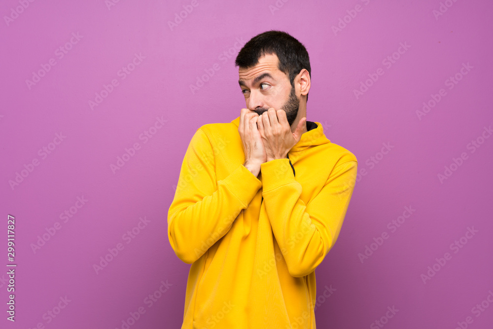 Handsome man with yellow sweatshirt nervous and scared putting hands to mouth Handsome man with yellow sweatshirt nervous and scared putting hands to mouth
