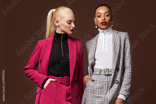 Two sexy beautiful woman fashion glamour model brunette blond hair makeup wear suit trousers jacket clothes every day casual office dress code party style accessory date walk skinny body shape studio.