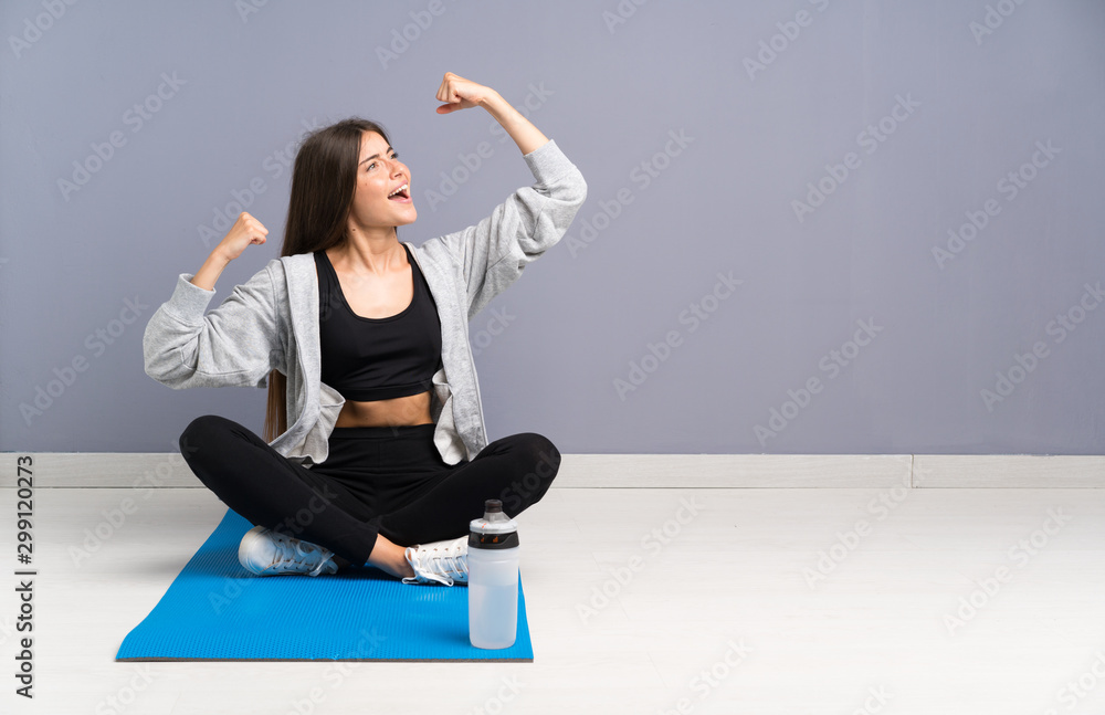 Fototapeta premium Young sport woman sitting on the floor with mat celebrating a victory