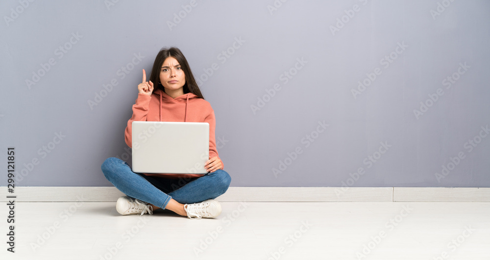 Young student girl with a laptop on the floor pointing with the index finger a great idea Young student girl with a laptop on the floor pointing with the index finger a great idea