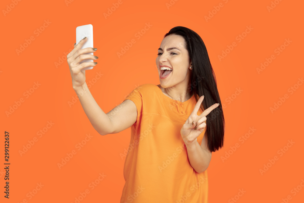 Caucasian young woman's portrait on orange studio background. Beautiful female brunette model in shirt. Concept of human emotions, facial expression, sales, ad. Copyspace. Making selfie, win in bet. Caucasian young woman's portrait on orange studio background. Beautiful female brunette model in shirt. Concept of human emotions, facial expression, sales, ad. Copyspace. Making selfie, win in bet.