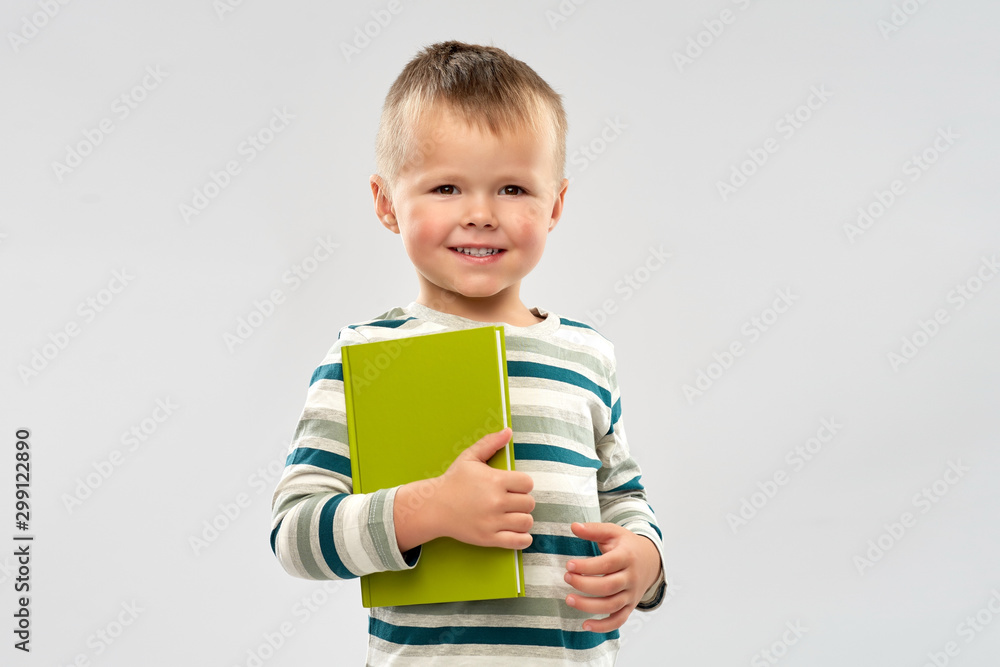 reading, education and childhood concept - portrait of smiling little boy holding book over grey background reading, education and childhood concept - portrait of smiling little boy holding book over grey background