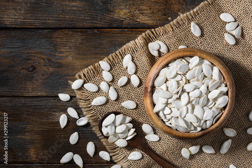 Raw pumpkin seeds in a wooden bowl on a wooden table. Top view with copy space