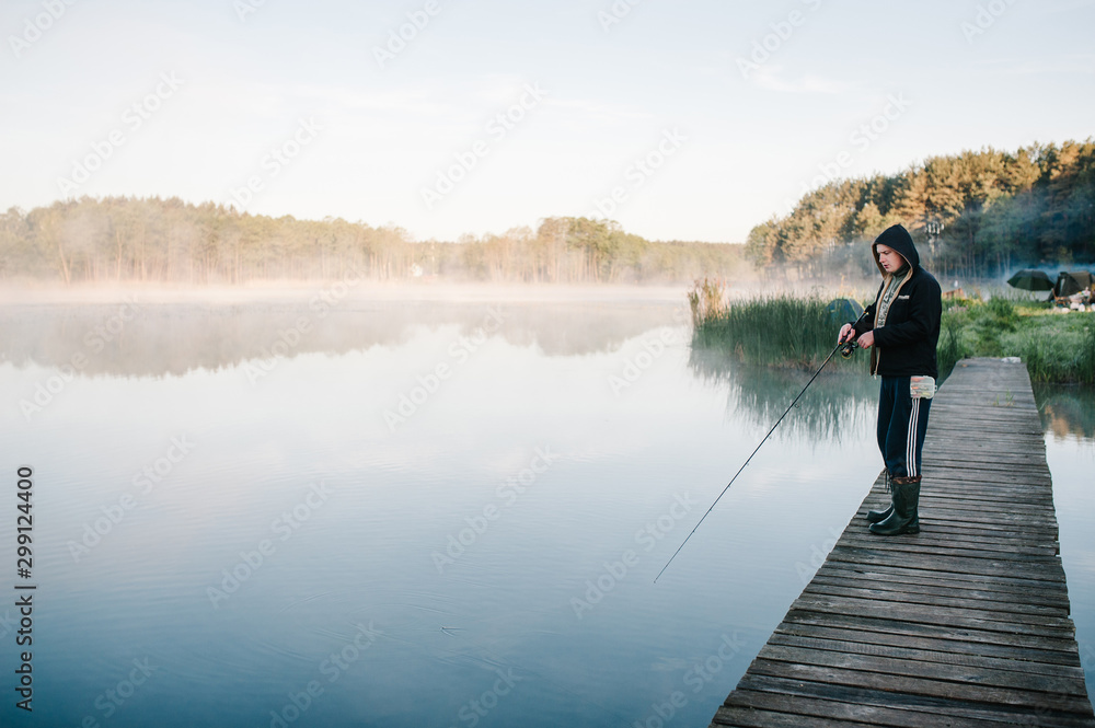 Fisherman with fishing rod on bridge. Sunrise. Fishing for pike, perch, crucian carp. Fog, grass, trees against the backdrop of lakes, nature. Fishing background. Misty morning. the wild nature. river
