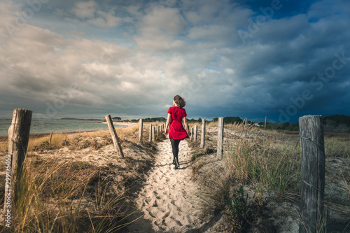 Girl in a red dress walking away on sand dunes
