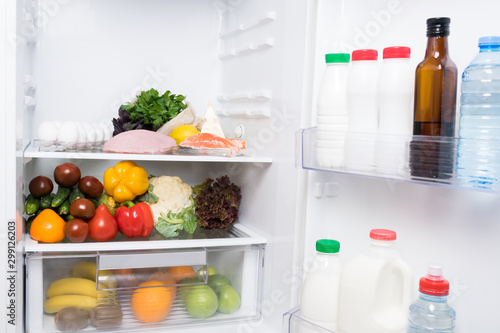 vegetables and fruits lie inside a white open refrigerator