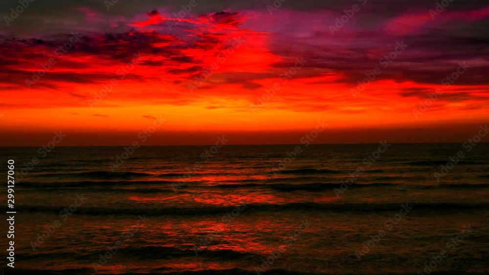 Sunrise over the sea. Fiery red sky and metallic gray water. Bright path to the shore.