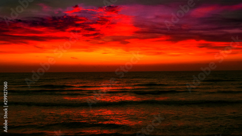 Sunrise over the sea. Fiery red sky and metallic gray water. Bright path to the shore.