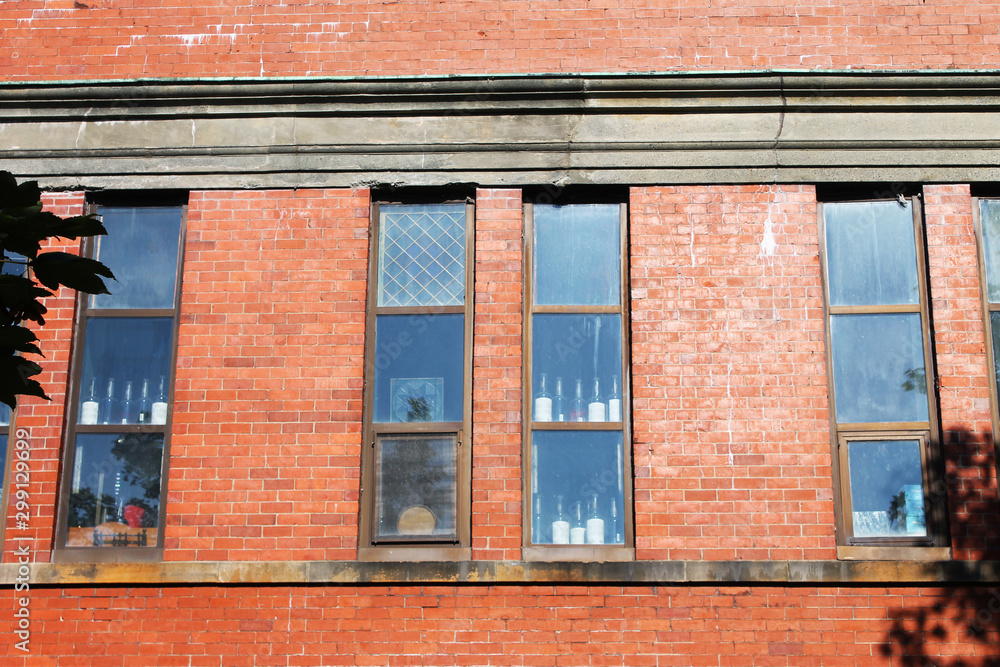 Windows in wall of old red brick building. Wine bottles are visible through the glass.