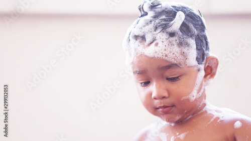2-year-old Asian child takes a bath and bubbles into his eyes, using his hands to rub his eyes. Happy toddler boy sitting at bathroom with foam. child playing with water by taking bath in bathtub.  
