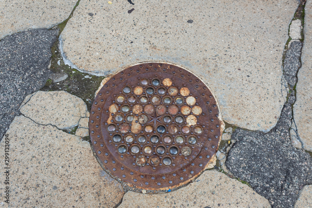Rusted iron and glass manhole cover set in crumbling concrete and asphalt sidewalk, horizontal aspect Rusted iron and glass manhole cover set in crumbling concrete and asphalt sidewalk, horizontal aspect