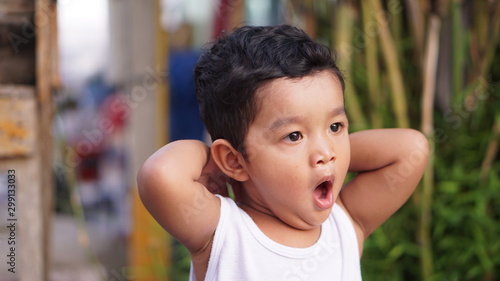 Foto Asian boy sitting near the water front, pretending to be sleepy and yawning with a wide mouth