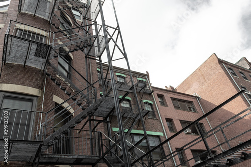 Layers of metal fire escapes on the exterior rear of old brick apartment building, horizontal aspect © Natalie Schorr