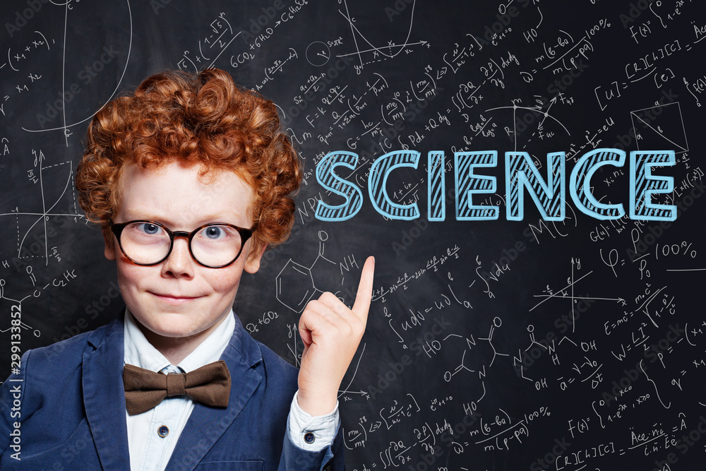 Confident kid little boy with ginger hair pointing at science inscription on chalkkboard background