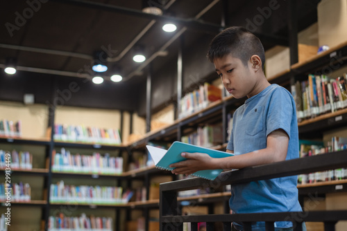 Asian boy student reading a book at the library in the school.Students search for books in the bookshelf.Portrait Asian boy.
