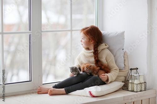 Little girl sitting on windows-sill with little kittens