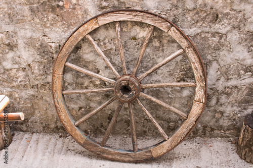 An old wooden cart wheel against a stone fence.