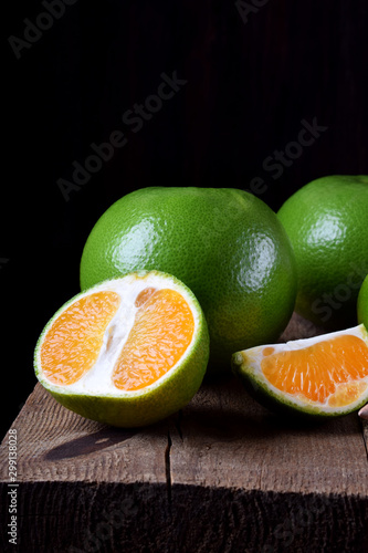 Green mandarins cut in halves and segments and whole sweetie on a wooden table