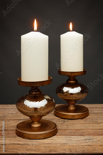 2 bronze candle holders and glowing candles, shot on a wooden table