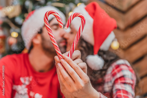 Closeup portrait of defocused amorous kissing couple holding a candy heart on the forefront.