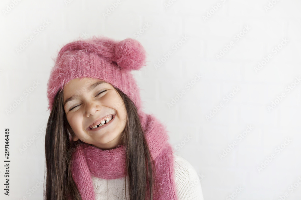 Winter portrait of happy child girl wearing knitted hat, snood and sweater. Toothless child girl having fun and laughing on light background. Fashion concept. Winter portrait of happy child girl wearing knitted hat, snood and sweater. Toothless child girl having fun and laughing on light background. Fashion concept.