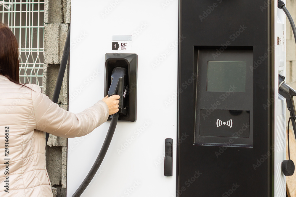 Woman use electrical fast charger to hybrid automobiles. High technology charger for green way of driving PHEV. Ecology friendly charger. New generation of environmental friendly green petrol station. Woman use electrical fast charger to hybrid automobiles. High technology charger for green way of driving PHEV. Ecology friendly charger. New generation of environmental friendly green petrol station.