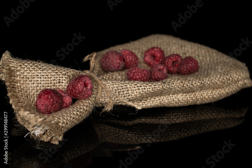 Lot of whole fresh crimson raspberry with jute bag isolated on black glass