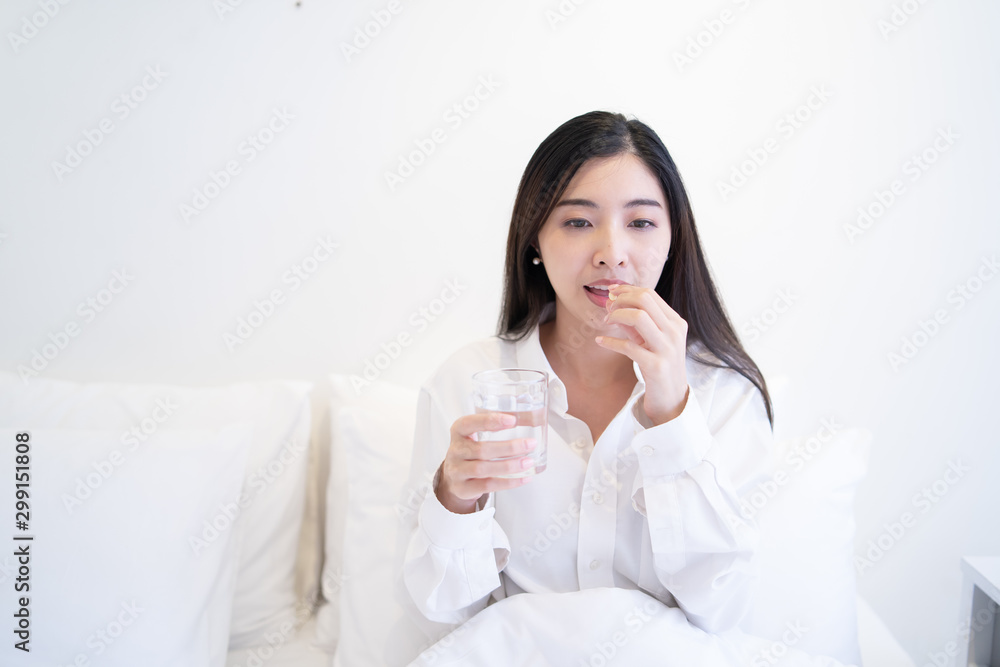 Young Thai girl Business woman taking medicine and drinking water,holding pills,glass of water on bed in hospital bedroom,she work hard while feels sick,drug remedy,health care Medical people concept Young Thai girl Business woman taking medicine and drinking water,holding pills,glass of water on bed in hospital bedroom,she work hard while feels sick,drug remedy,health care Medical people concept