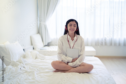 chill out relax and leisure concept, Beautiful young Thai Asian woman with headphone or earphone relaxing on the bed, she is listening to music using a tablet and lying down with eyes closed bedroom