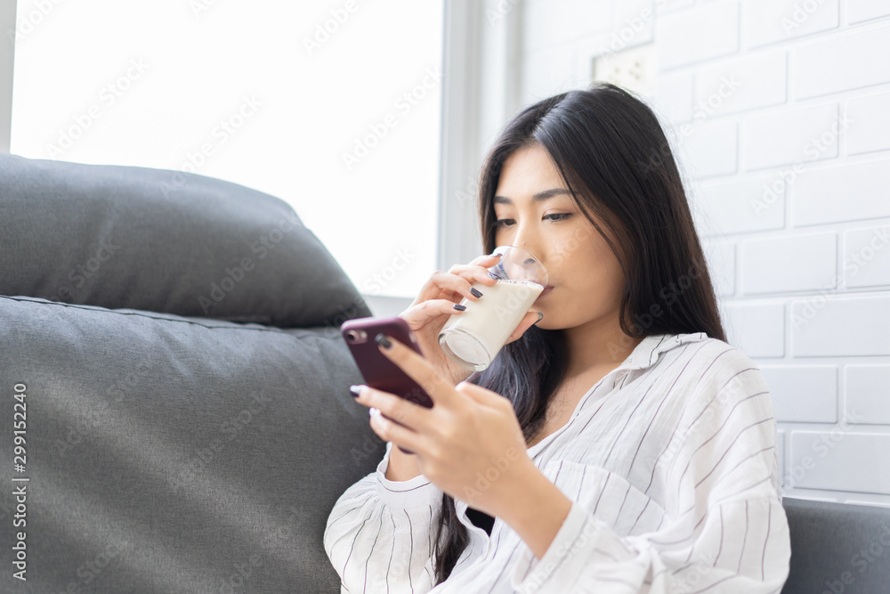 Happy young Asian woman drinking milk from the glass after exercise.over white background, shake looking at camera in the living room at home Happy young Asian woman drinking milk from the glass after exercise.over white background, shake looking at camera in the living room at home