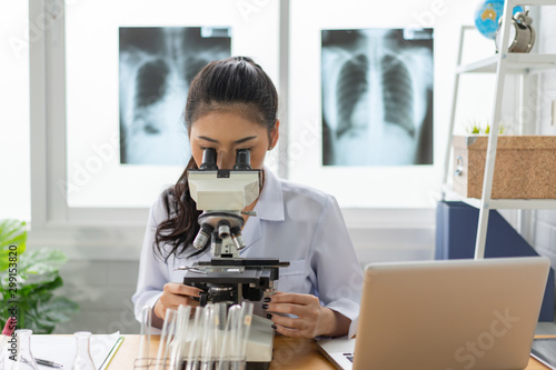 Photography Asian female doctor working on laptop with a microscope for an exam at hospital