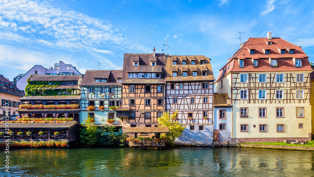 Panoramic front view of typical half-timbered buildings with pastel facades lining the river Ill in the Petite France quarter in Strasbourg, France, on a sunny morning.