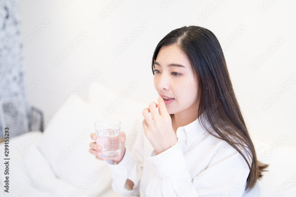 Young Thai girl Business woman taking medicine and drinking water,holding pills,glass of water on bed in hospital bedroom,she work hard while feels sick,drug remedy,health care Medical people concept Young Thai girl Business woman taking medicine and drinking water,holding pills,glass of water on bed in hospital bedroom,she work hard while feels sick,drug remedy,health care Medical people concept