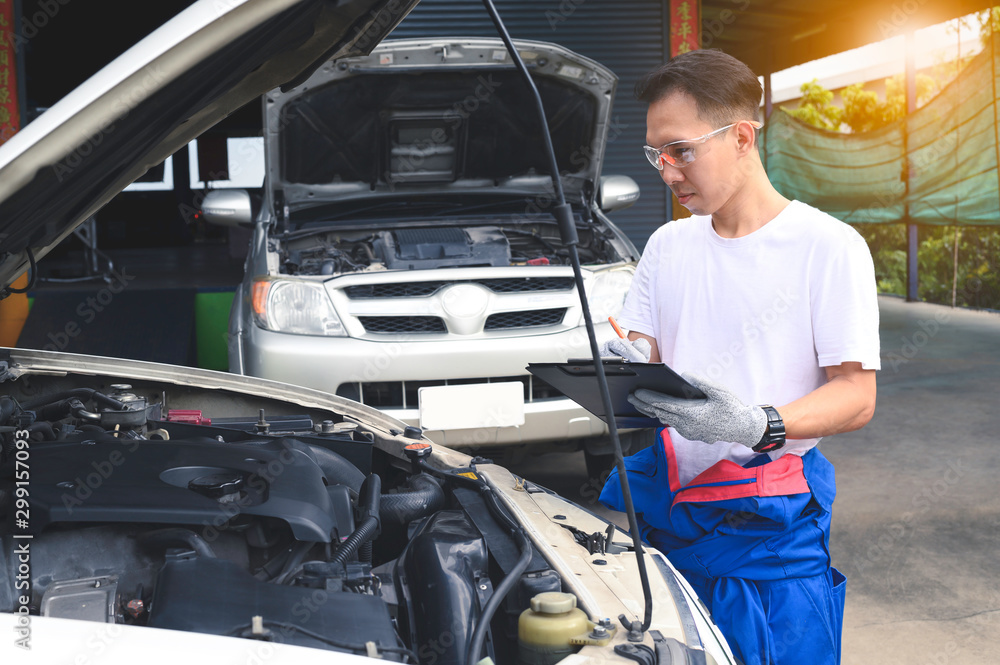 Mechanic is checking the engine and analyzing the car engine problem and writing to clipboard. Checklist for machine repair, car service and maintenance. Mechanic is checking the engine and analyzing the car engine problem and writing to clipboard. Checklist for machine repair, car service and maintenance.