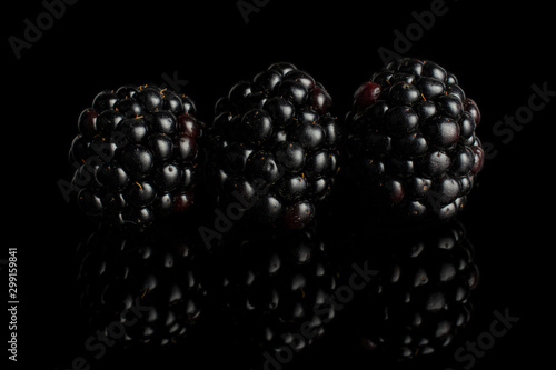 Group of three whole fresh black blackberry in row isolated on black glass