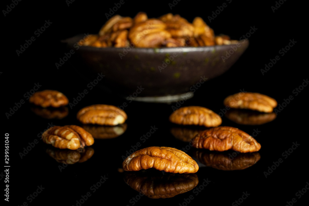 Lot of whole dry brown pecan nut in dark ceramic bowl isolated on black glass Lot of whole dry brown pecan nut in dark ceramic bowl isolated on black glass