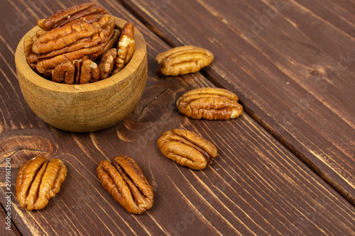 Lot of whole dry brown pecan nut in tiny wooden bowl on brown wood