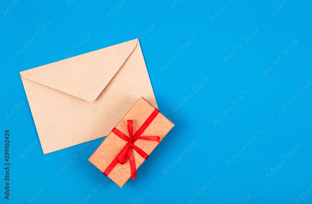 Top view of simple gift box decorated with red bow ribbon and craft envelope on blue background. Flat lay. Minimal concept. . Top view of simple gift box decorated with red bow ribbon and craft envelope on blue background. Flat lay. Minimal concept. .