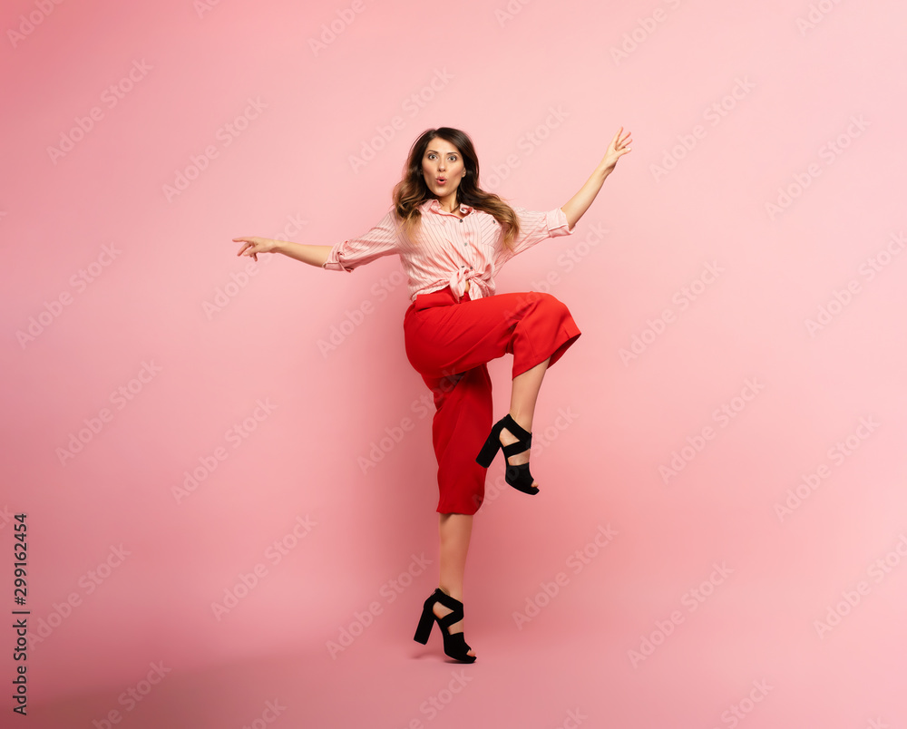 Brunette girl with red clothes jumps over a pink background. Concept of fashion and shopping with joyful expression