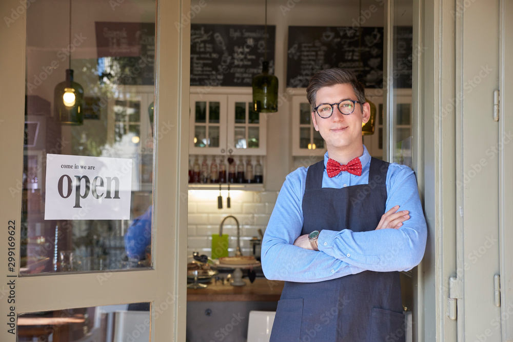 Fototapeta premium Small business owner standing in the cafe entrance with open sign while wating for guest