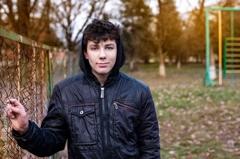 Teenager resting after a grueling workout on the street in early winter, boy tired but happy. The guy is wearing a black jacket and a hood on his head