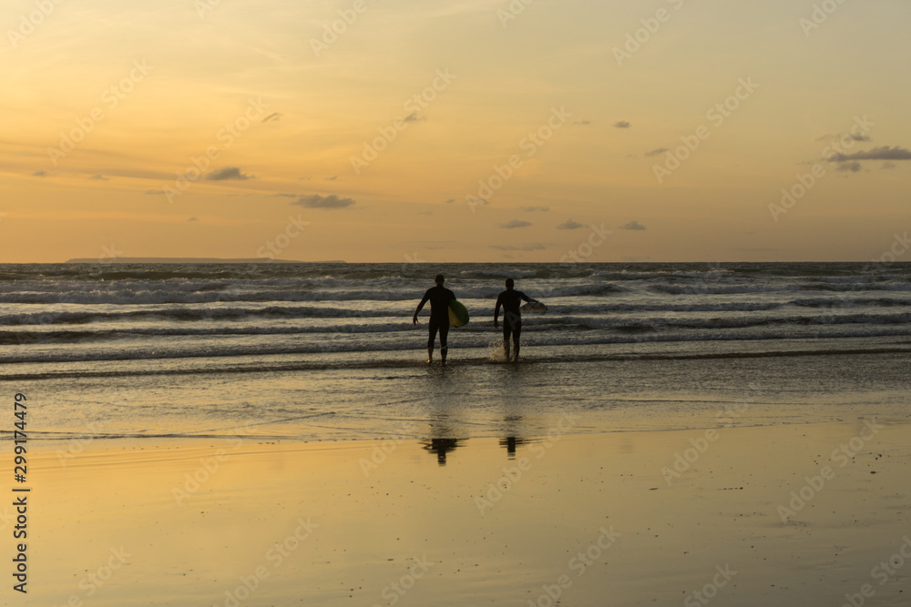 sunset surfers heading out to catch some waves at Westward Ho in Devon