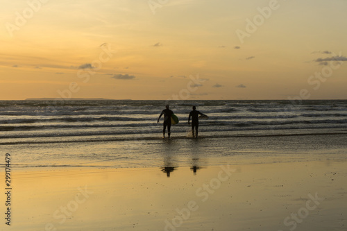 sunset surfers heading out to catch some waves at Westward Ho in Devon