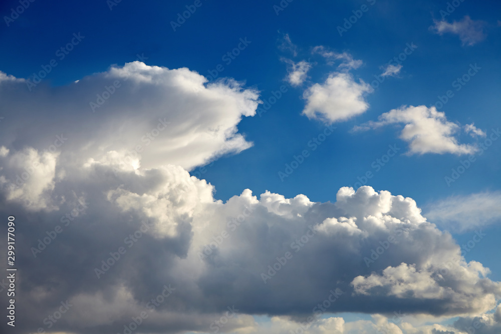 Naklejka premium Blue sky with a big white clouds in the light of the sun. Large fluffy cumulonimbus clouds at sunny day. Meteorology, weather forecast