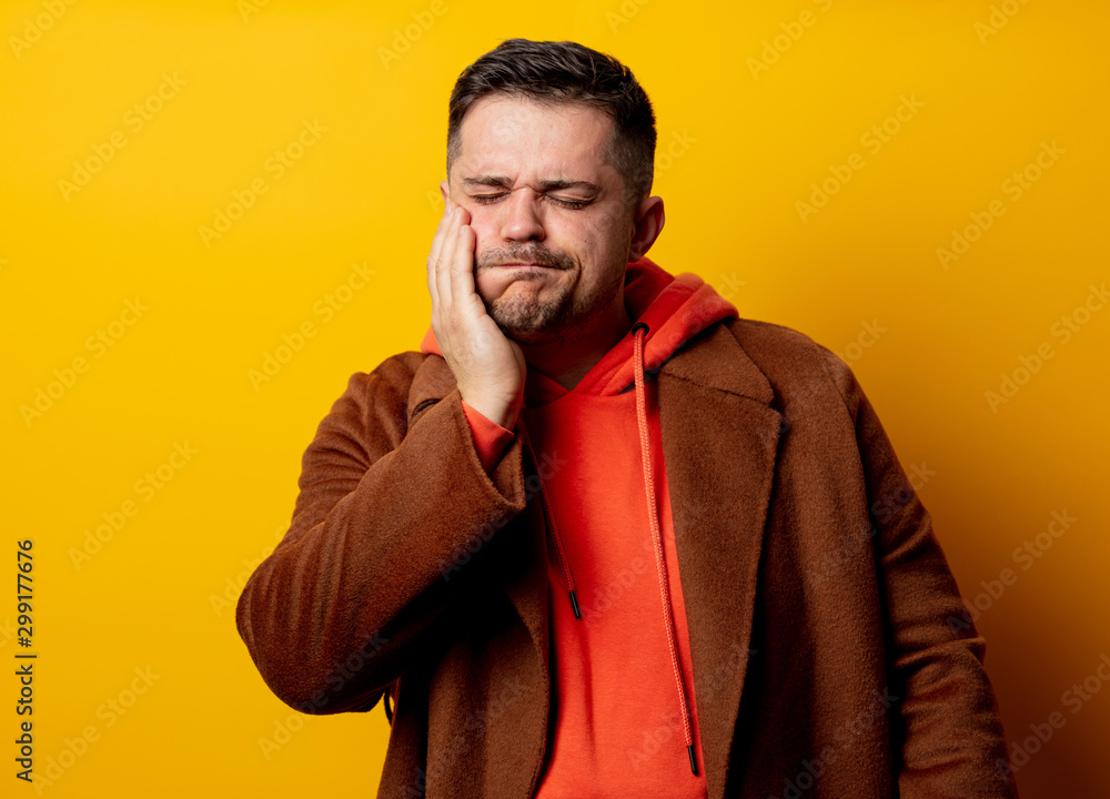 Angry man in coat with tooth pain on yellow background Angry man in coat with tooth pain on yellow background