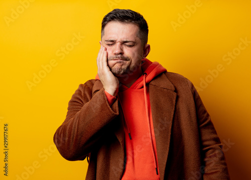 Angry man in coat with tooth pain on yellow background