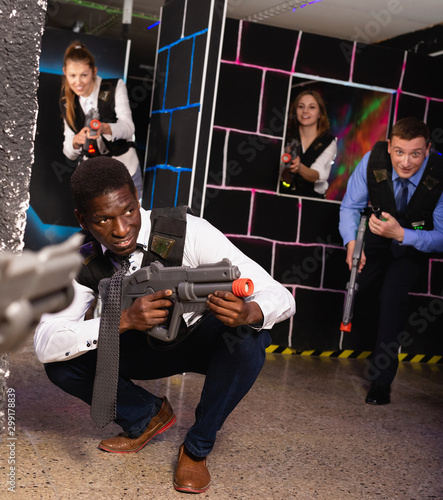 Men and women in business suits playing laser tag emotionally in dark room