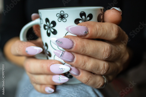 Women s hands with manicured nails holds cup of coffee