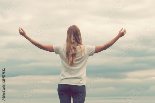 Beautiful girl on the lake. The view from the back. Hands up. Cloudy sky, sunset