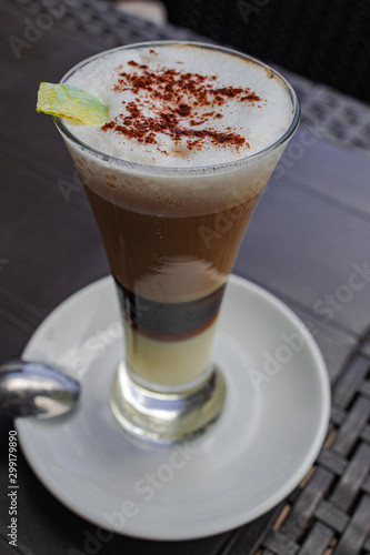 Coffee with milk, liqueur, cinnamon and lemon, in a glass on a black table